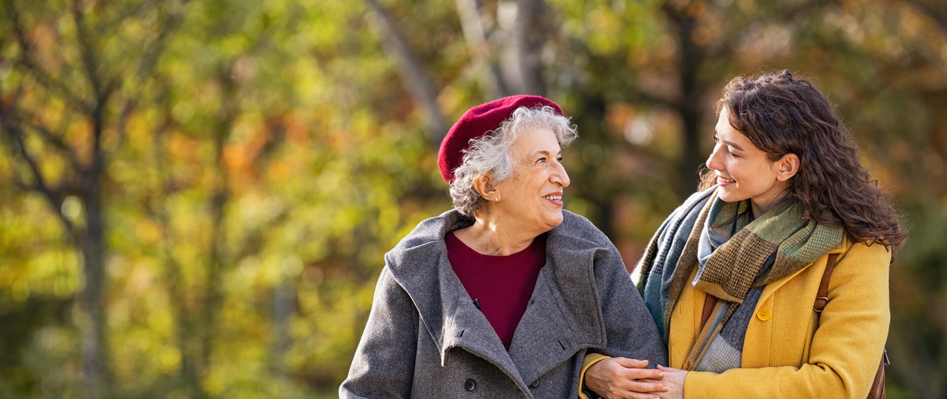 An older woman and her adult daughter walking arm in arm outdoors in autumn